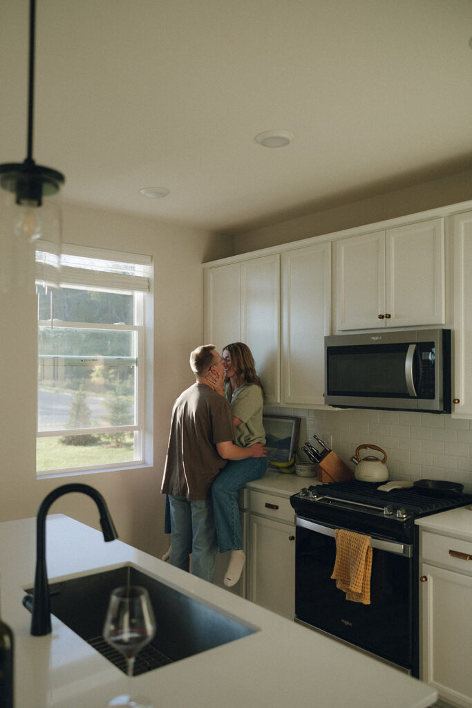 Man kisses his wife as she sits on kitchen counter