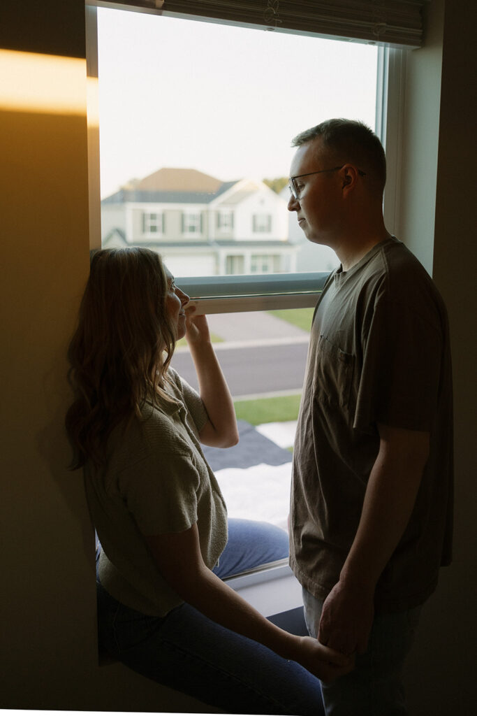 Man gazes down at his wife as they sit in the windowsill of their home