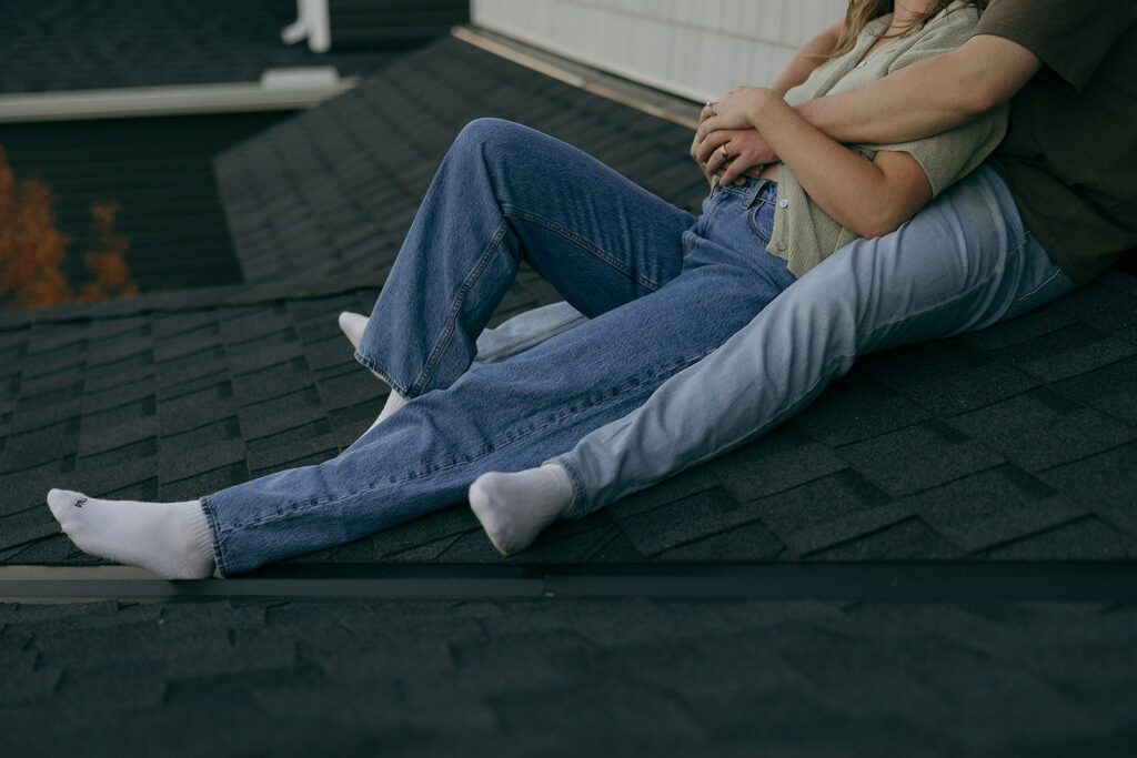 Couple wearing denim jeans and white socks lays together on rooftop of their Minnesota home