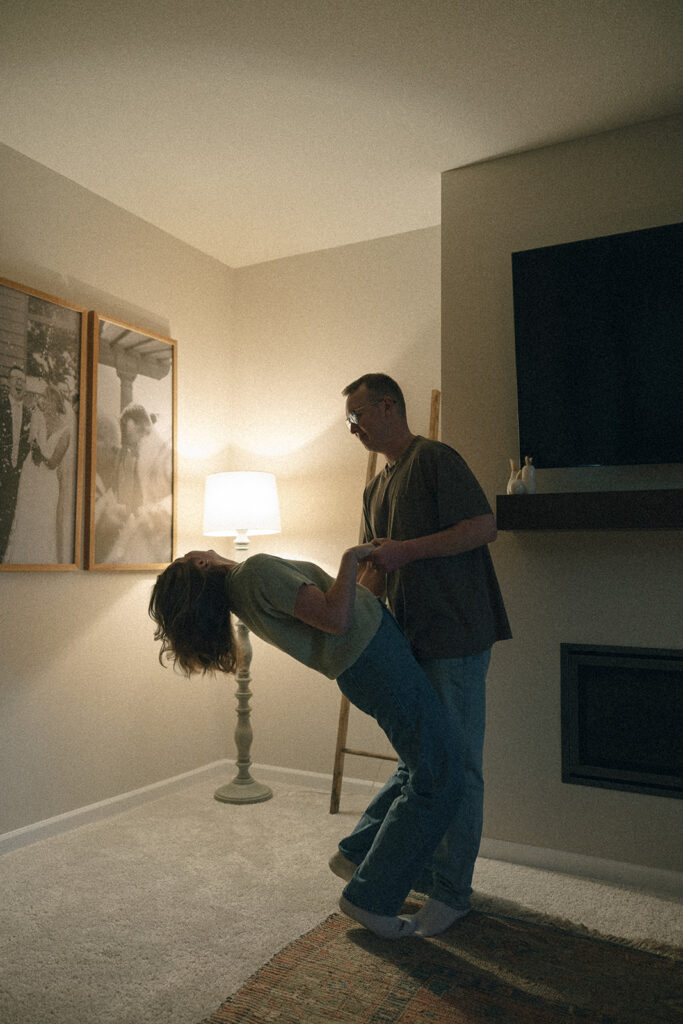 Man dips his wife as they slow dance through their dimly lit living room