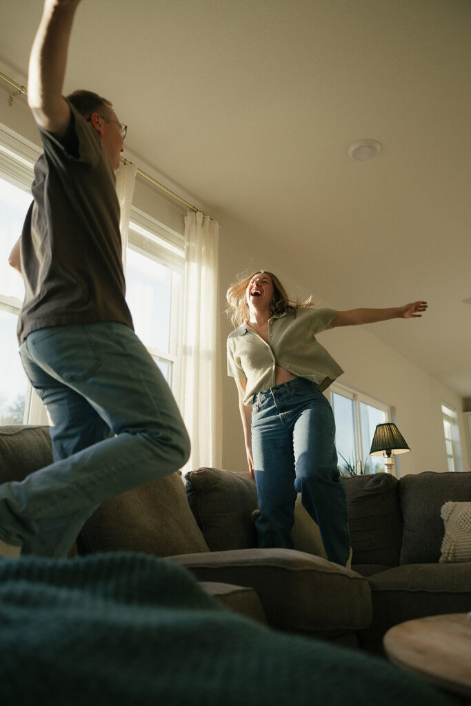 Man and woman in denim jeans jump on couch in Minnesota couples photography session