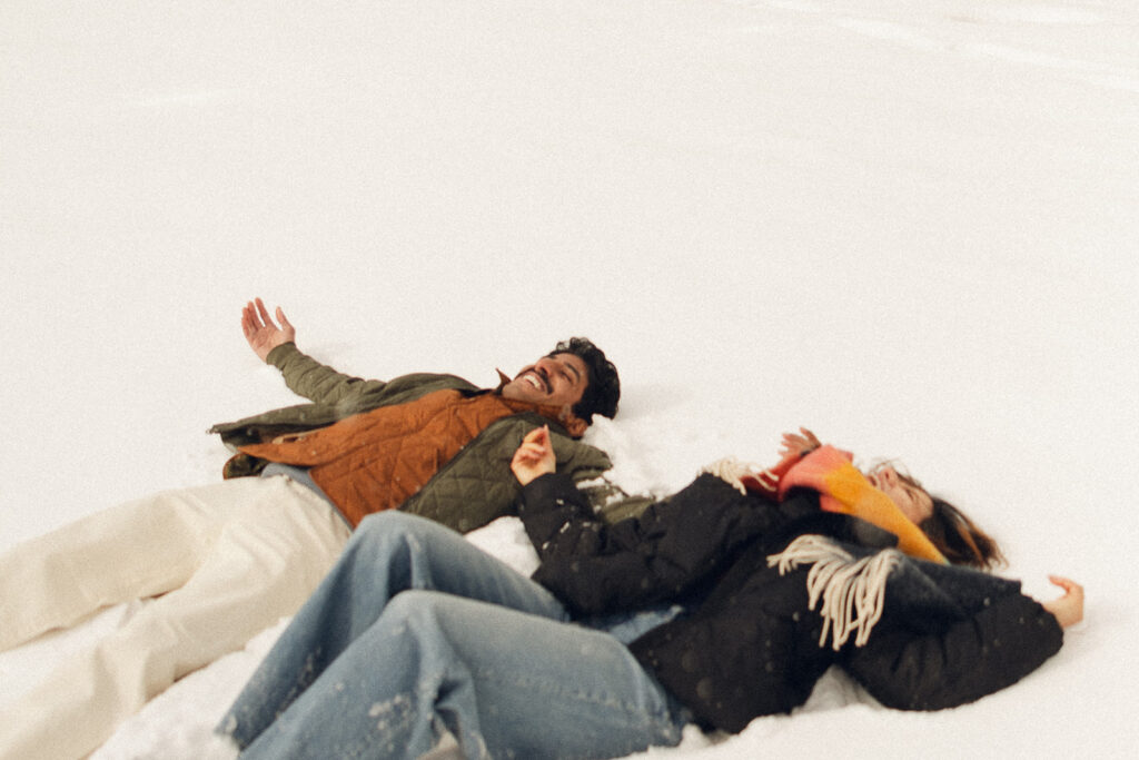 Couple laying in the Minnesota snow, sheer joy etched on their faces