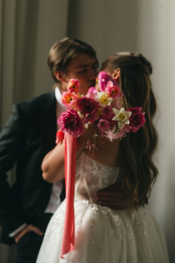 Bridal bouquet hides newlyweds' faces as they share an intimate kiss.