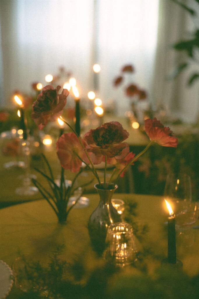Single stem flowers sit in silver vases while candlelight bounces off of them