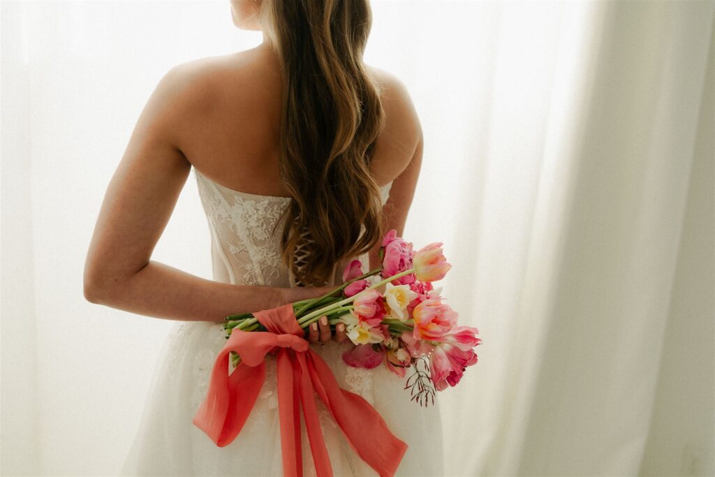 Bride holds her vibrant, bow-tied bouquet behind her back at microwedding