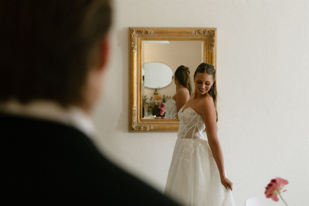 Bride shows off her dress as groom admires in the foreground