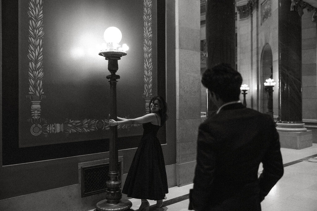 Woman twirls around lamppost while looking over her shoulder at man