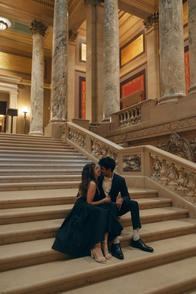 Couple cuddles on Capitol steps with dramatic architecture surrounding them