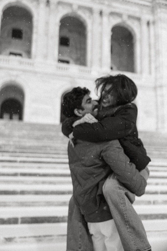 Abhi lifts Shubhi in the air, surrounded by soft Minnesota snowfall
