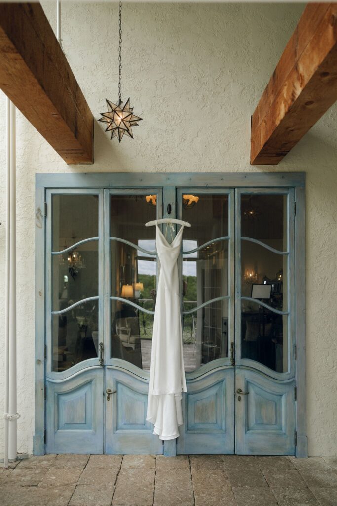 Bridal gown displayed in front of blue doors beneath starburst chandelier.