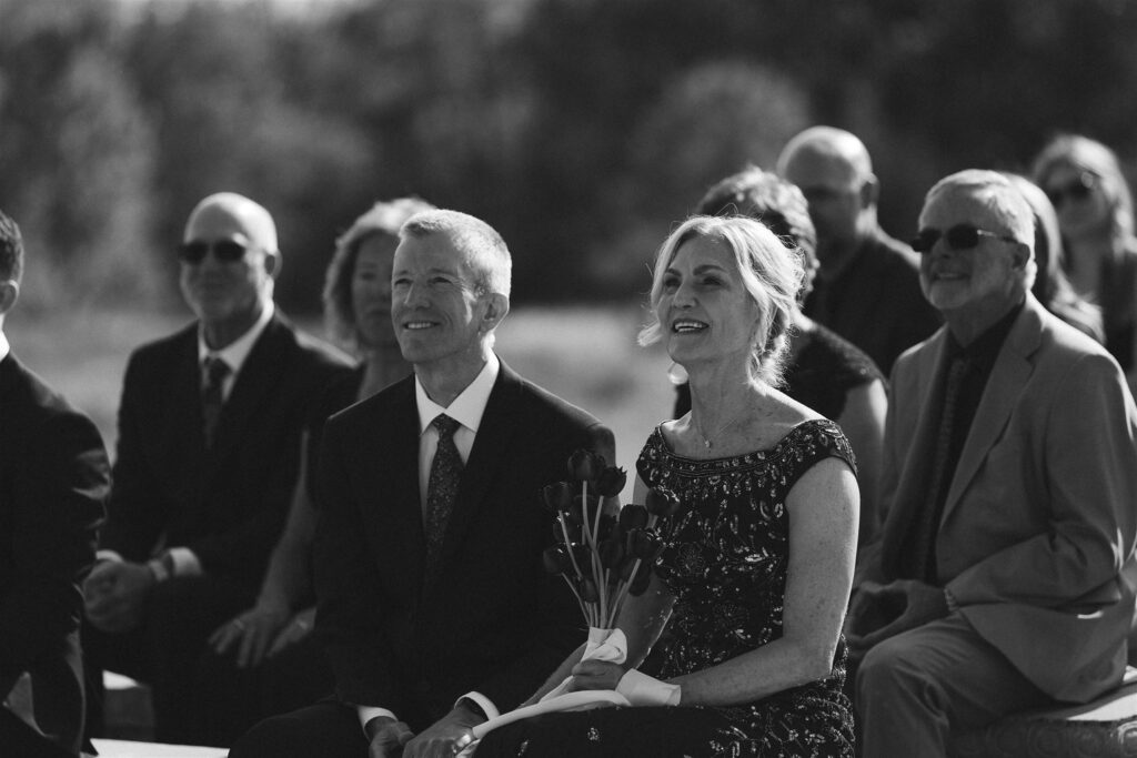 Parents of the bride smiling from the front row during ceremony at Edward Anne Estate.