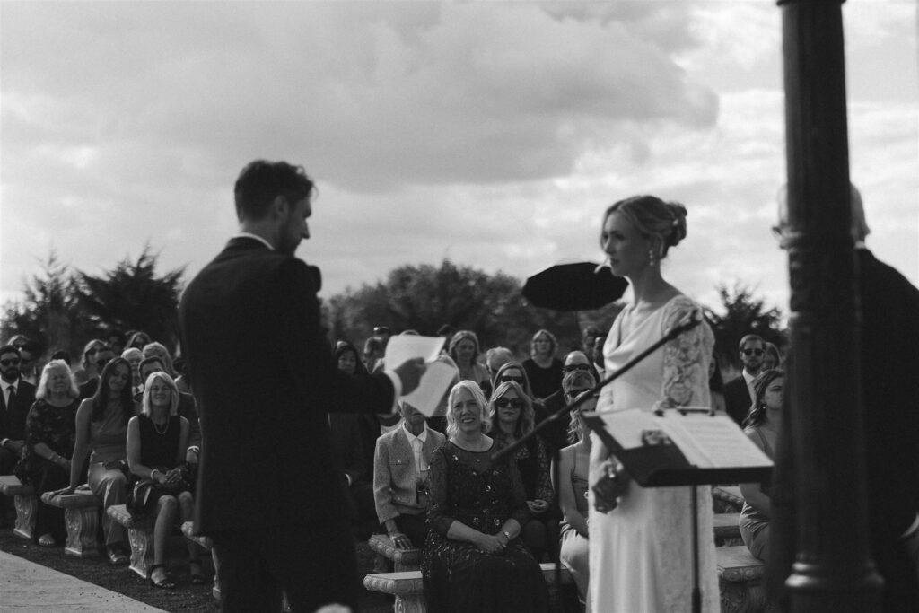 Bride and groom exchanging vows outdoors as guests look on