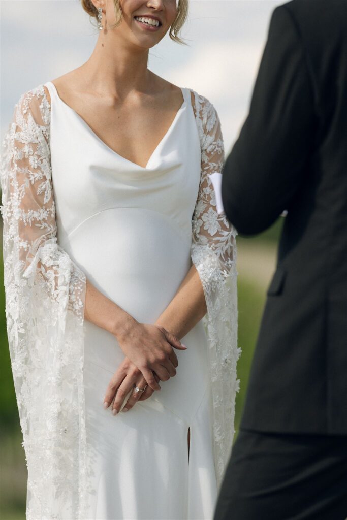 Bride smiling in lace-trimmed robe during outdoor vows at Minnesota wedding