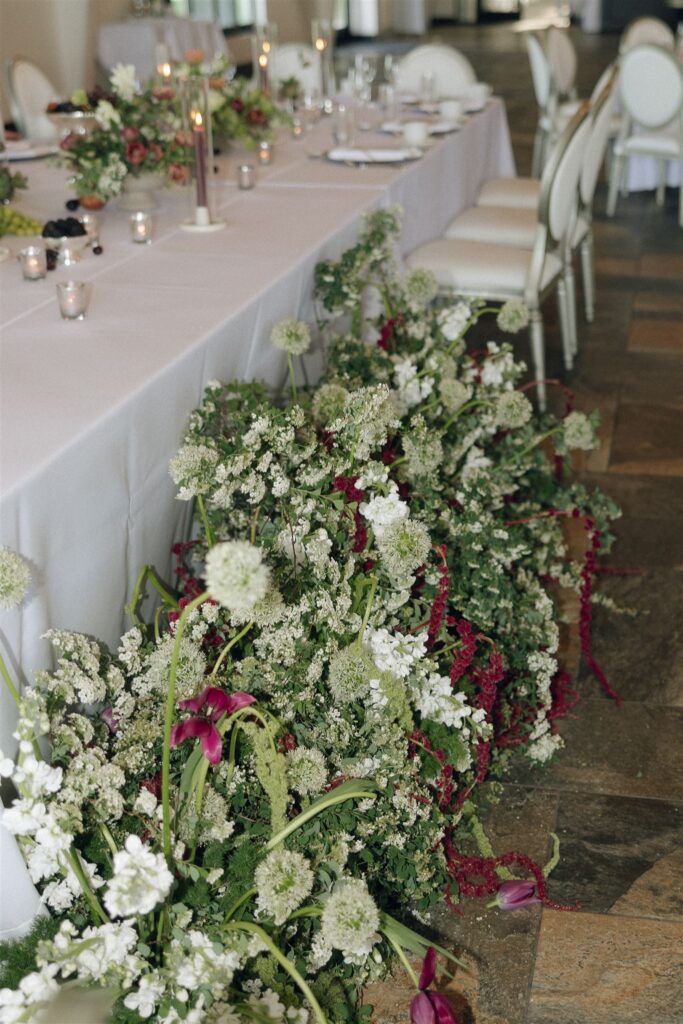 Floral-filled head table installation with green and burgundy blooms.