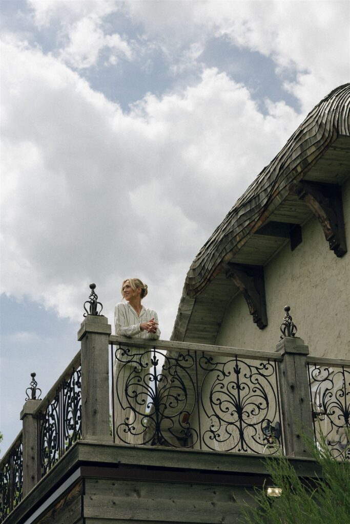 Bride on the Juliet balcony at Edward Anne Estate, overlooking the ceremony lawn with European flair