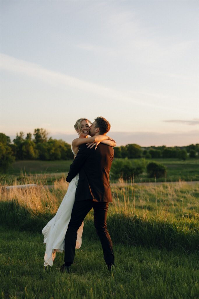 Couple shares a playful lift and spin at golden hour in an open field.