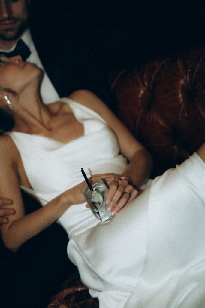 Candid moment of the bride laughing, cocktail in hand, reclined against groom.