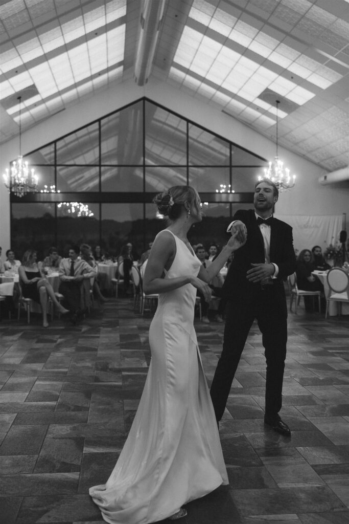 Bride and groom share their first dance in a bright, glass-ceilinged reception space.