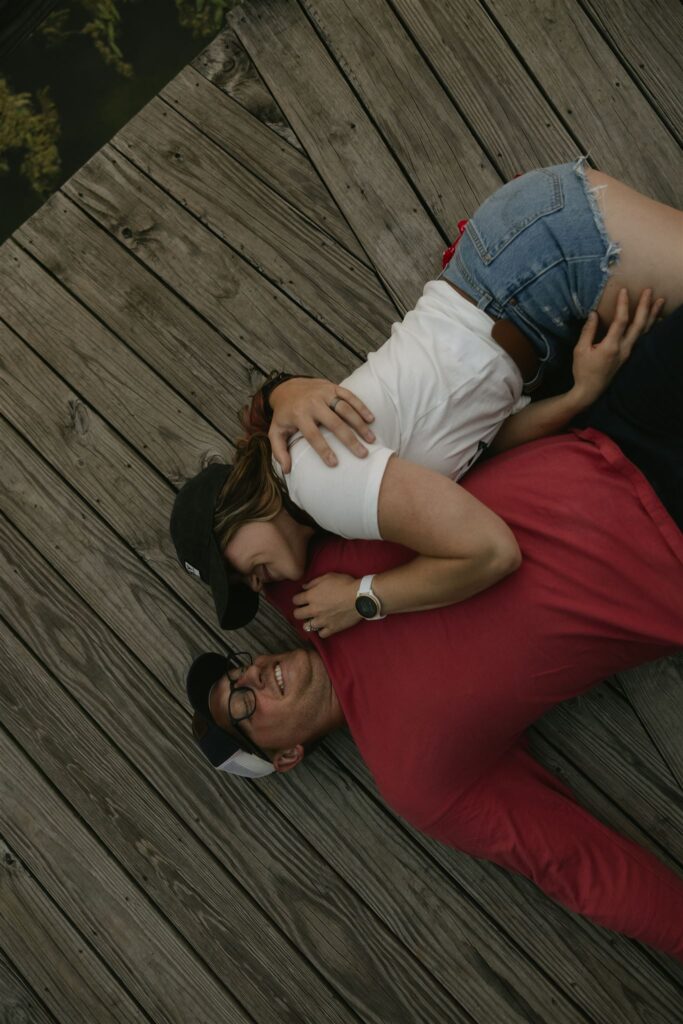 Couple lying together on a wooden boardwalk, laughing.