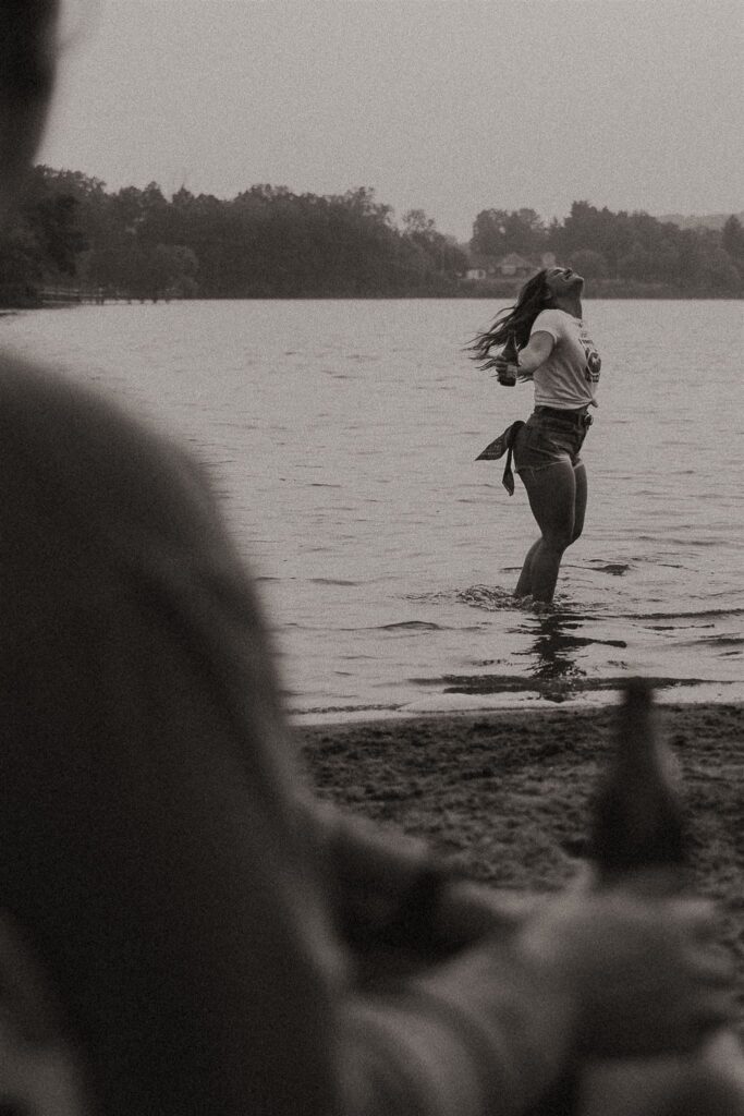 Blurred view of beer bottle in hand with woman running into the water in the background for summer engagement photos