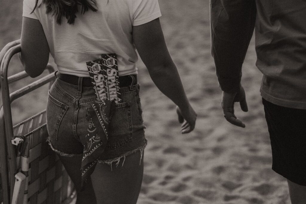 Rear view of couple walking on the sand, her red bandana in back pocket.
