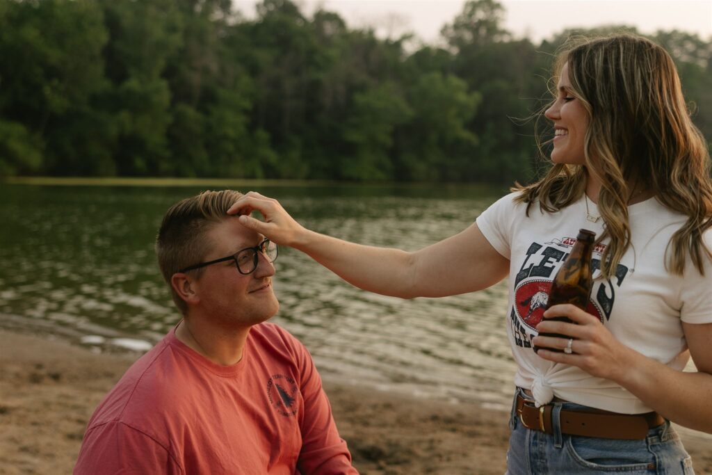 Woman smiling while running her hand through man’s hair as he sits with a beer.