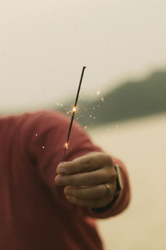 Close-up of hand holding a lit sparkler on the beach for  summer engagement photos