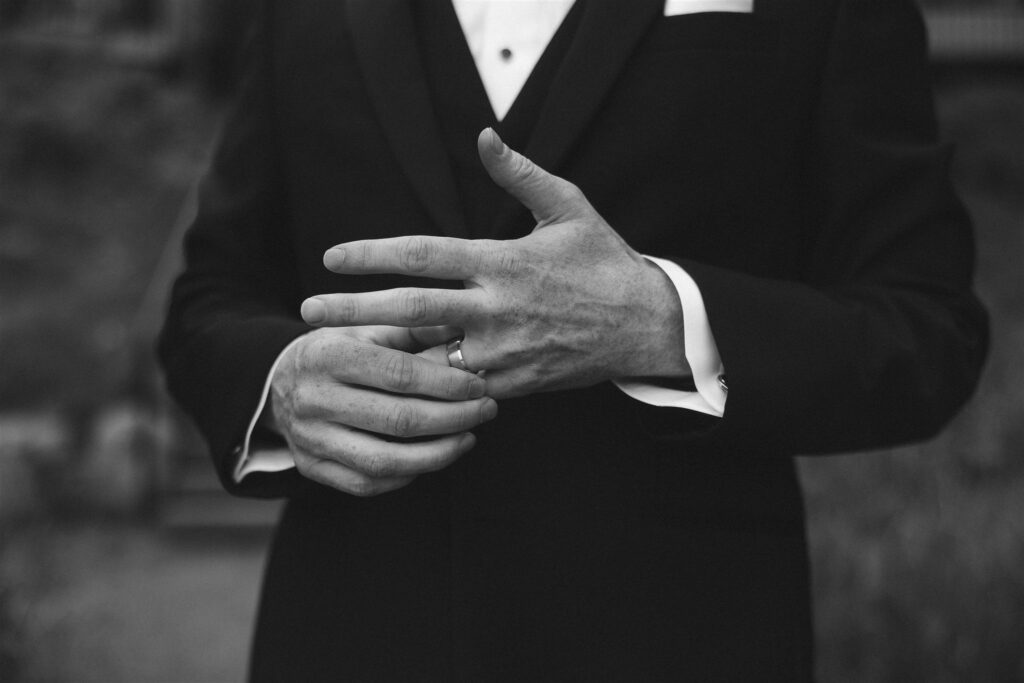 Close-up of groom adjusting his wedding ring in a classic black suit.