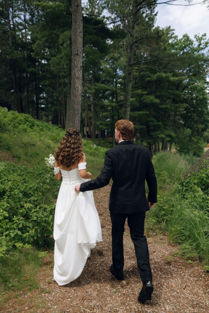Bride and groom walking together on a wooded path in Nisswa, MN in documentary style wedding photos.