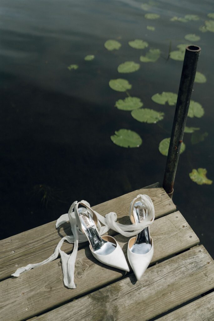 White bridal shoes resting on a dock above lily pads on Clark Lake.