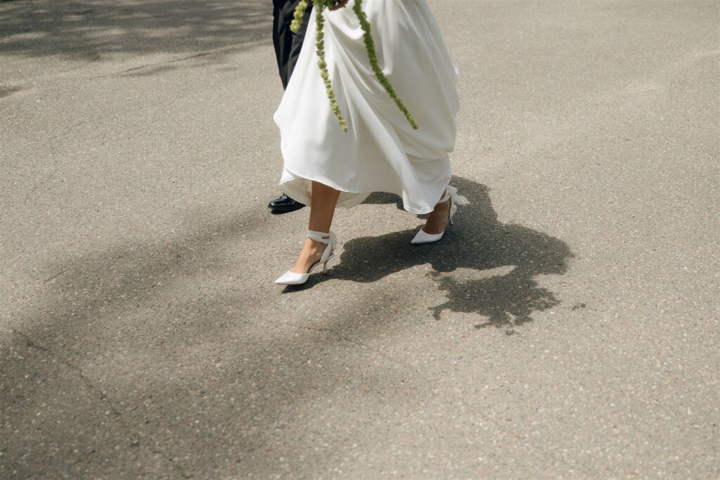 Bride walking down the road in heels with her bouquet trailing — candid wedding moment.