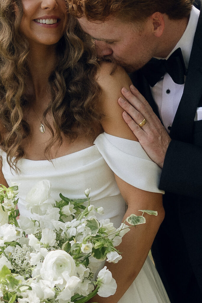 Close-up of the groom kissing the bride's shoulder.