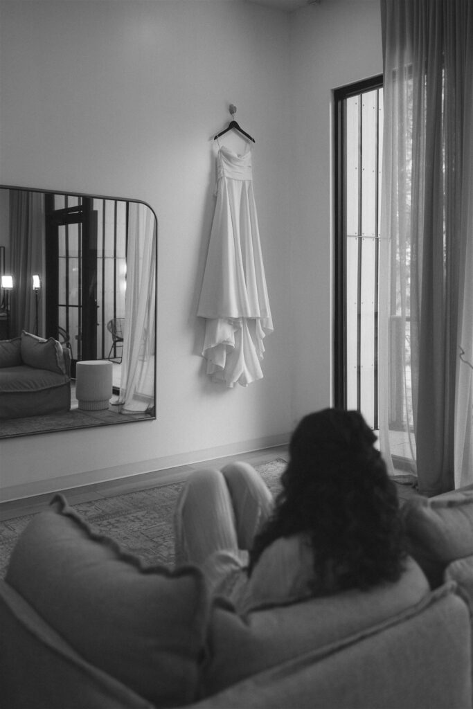 Bride sitting on a couch watching her gown by the window in documentary style wedding photos.