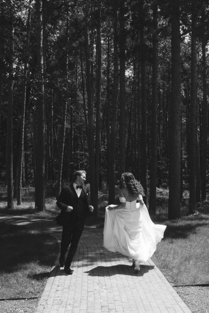 Bride and groom walking beneath tall pine trees at Catalyst at Nature Link.