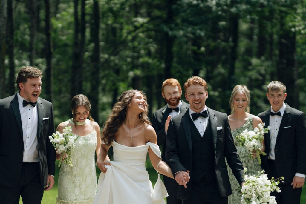 Full wedding party walking arm in arm through the woods.