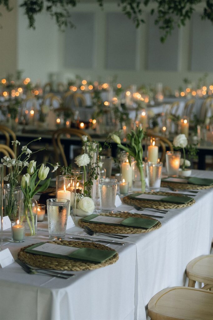 Candlelit reception tables with greenery and glowing taper candles inside Catalyst at Nature Link for documentary style wedding photos.