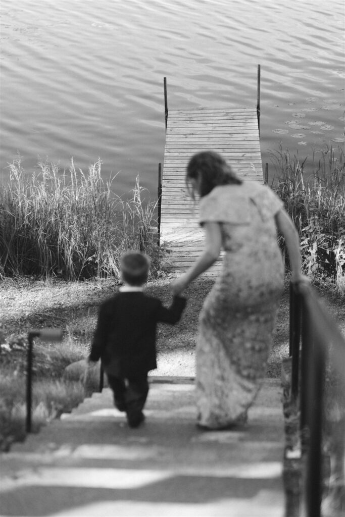 Guest walking hand in hand with a young child down to the dock on the lake in documentary style wedding photos.