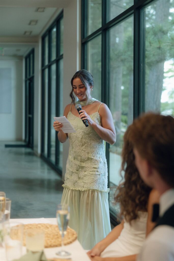 Maid of honor giving her toast in front of tall windows.