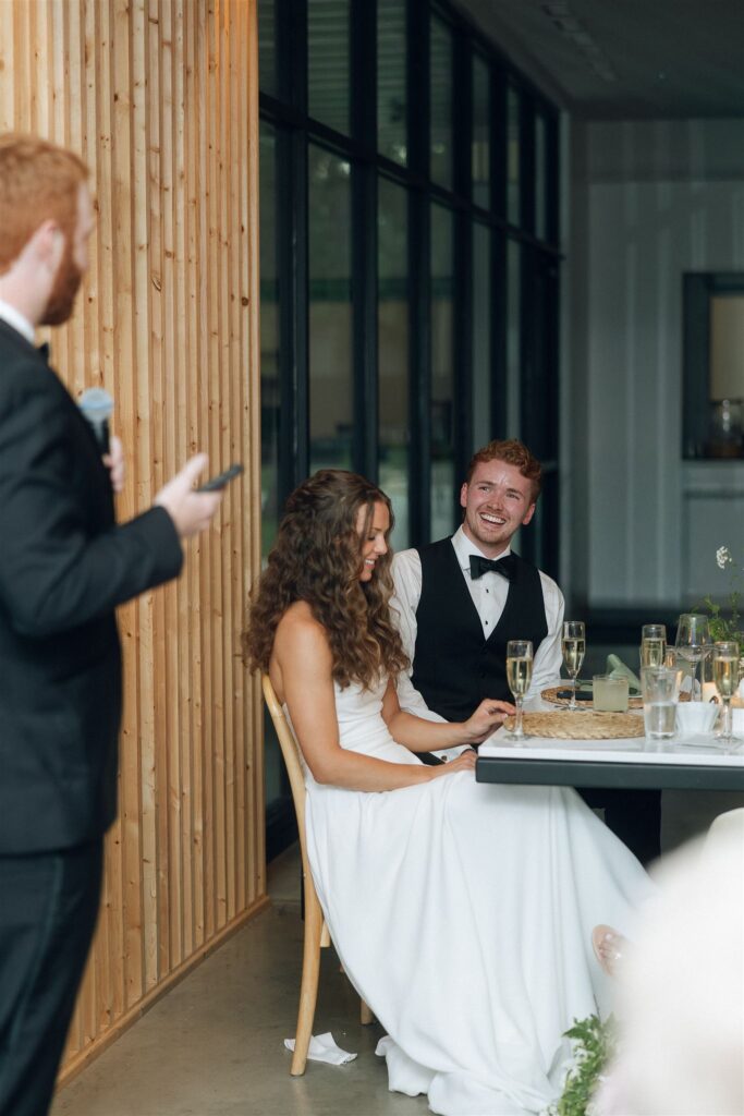 Groom laughing during best man's speech in documentary style wedding photos.