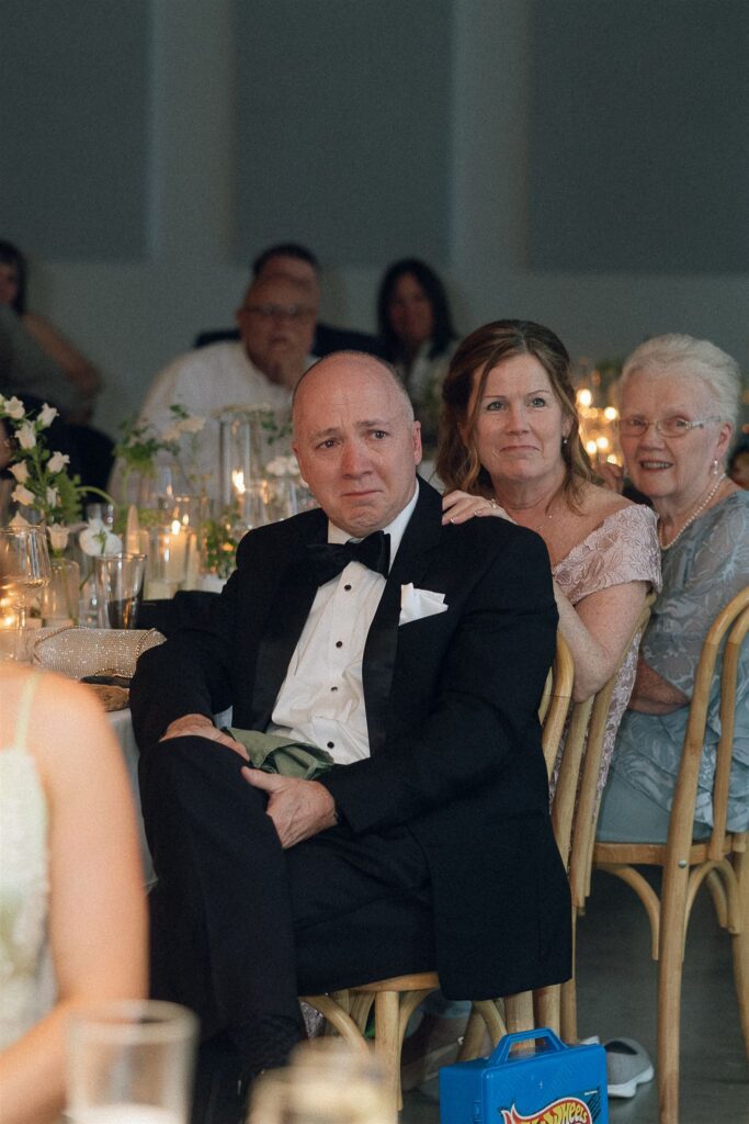 Groom’s parents crying while seated at the reception.