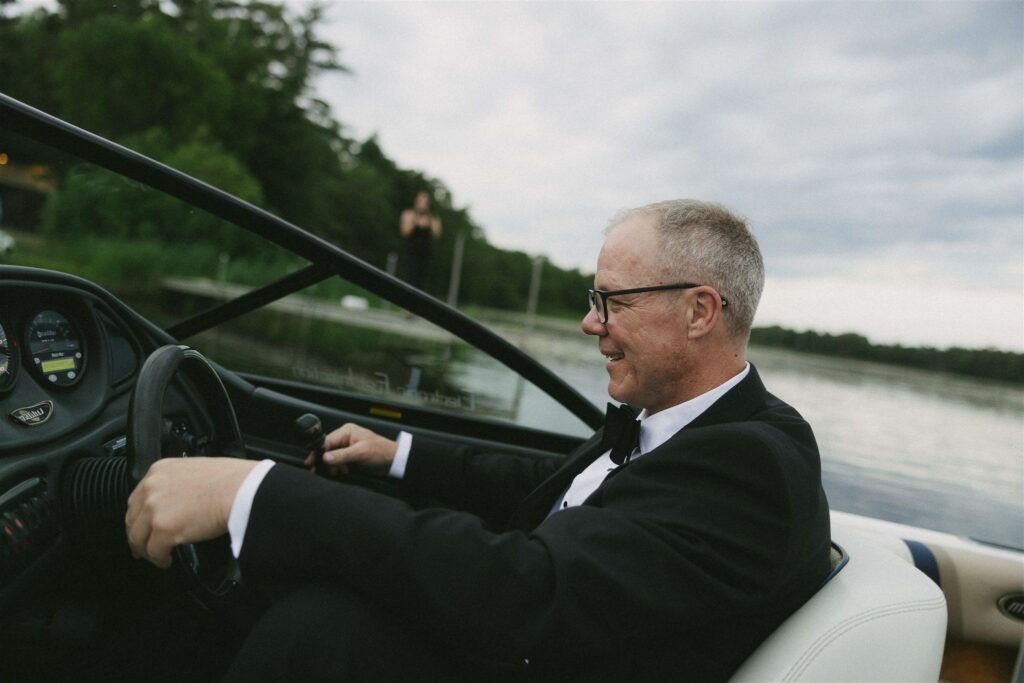 Father steering the boat across Clark Lake in authentic storytelling wedding photography.