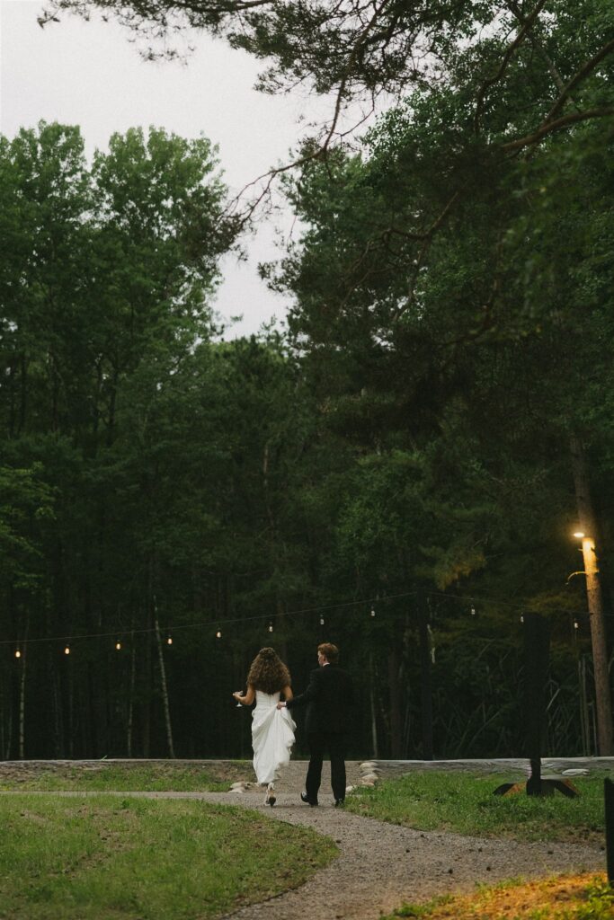 Bride and groom walking arm in arm along the path outside Catalyst at night with string lights glowing in documentary style wedding photos.