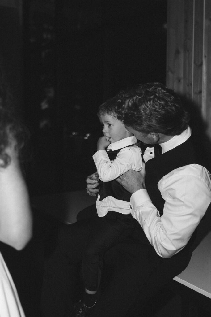 Groom holding a toddler on their lap during reception, candid storytelling moment in documentary style wedding photos.
