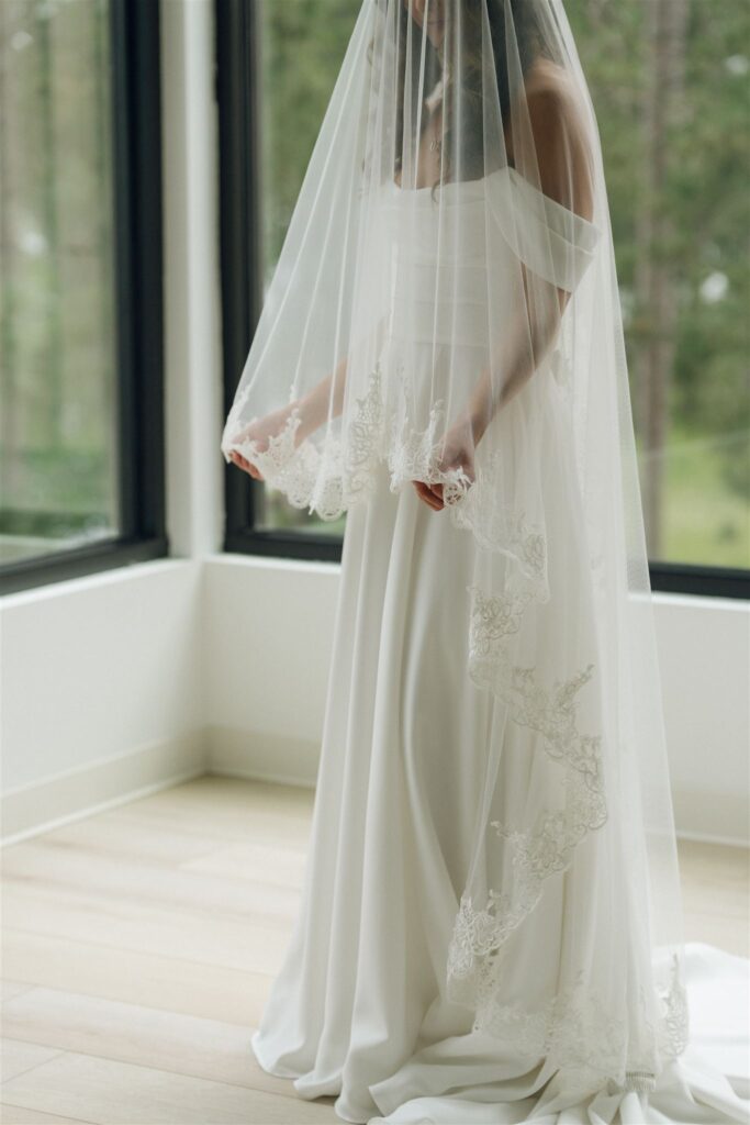 Bride adjusting her veil by a window at Catalyst at Nature Link.
