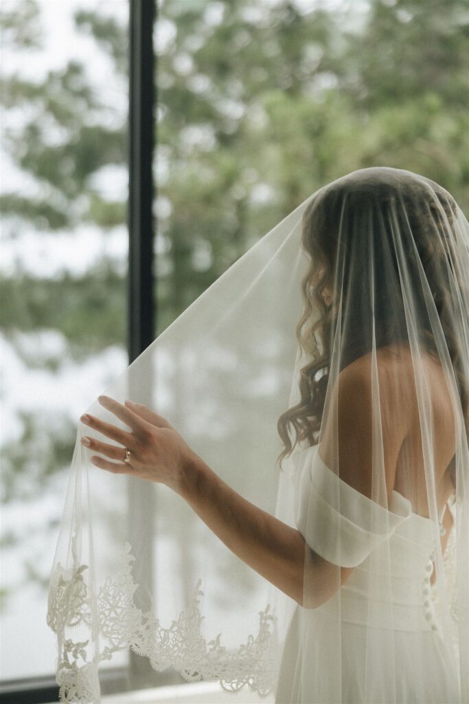 Bride adjusting her veil in front of a window before the ceremony.
