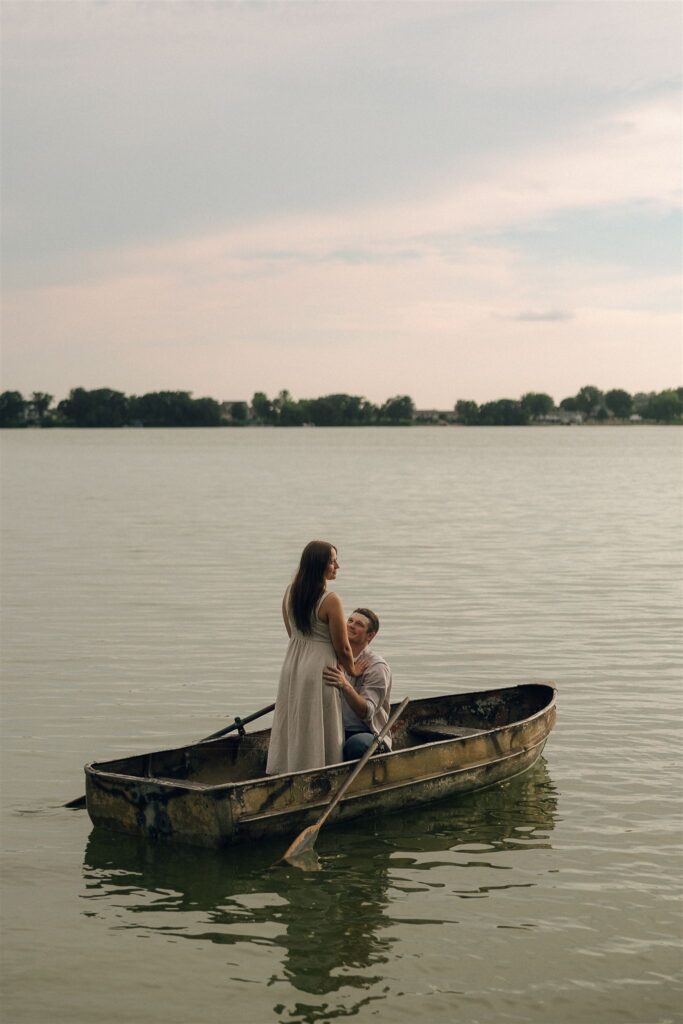 Sophie standing in the small boat while Jake looks up at her, the moment still and romantic against the open lake.