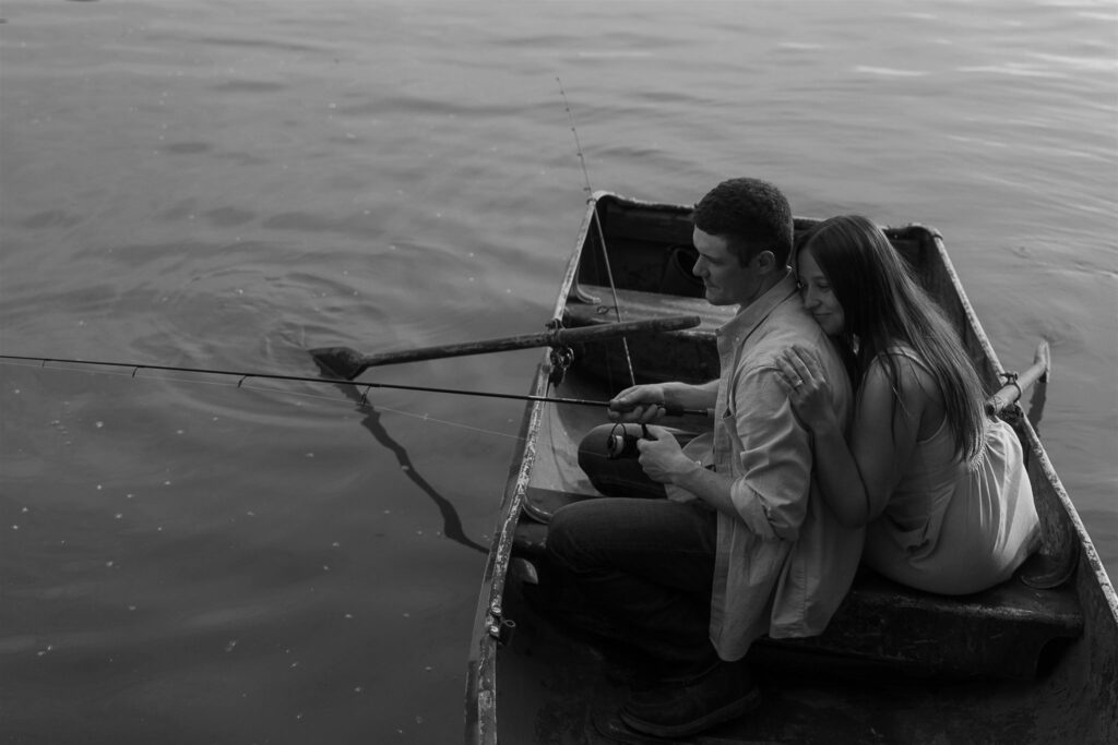 Sophie rests her head against Jake's back while he fishes off the rowboat in storytelling engagement photos.