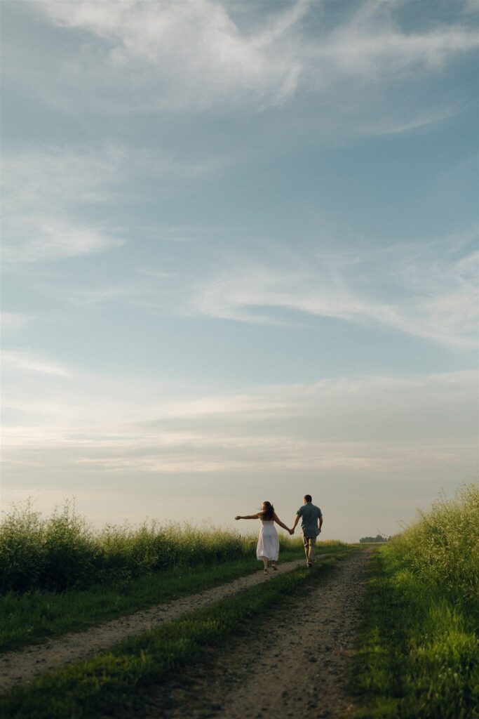 Sophie and Jake run hand-in-hand down a gravel road under an open summer sky, laughter and motion turning this Minnesota engagement session into something straight out of a film.