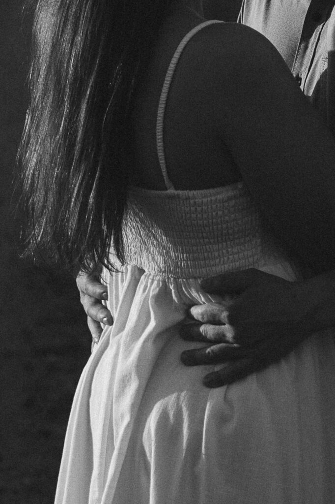 Black and white close-up of Jake’s hands around Sophie’s waist, light and shadow tracing quiet intimacy for their storytelling engagement photos.