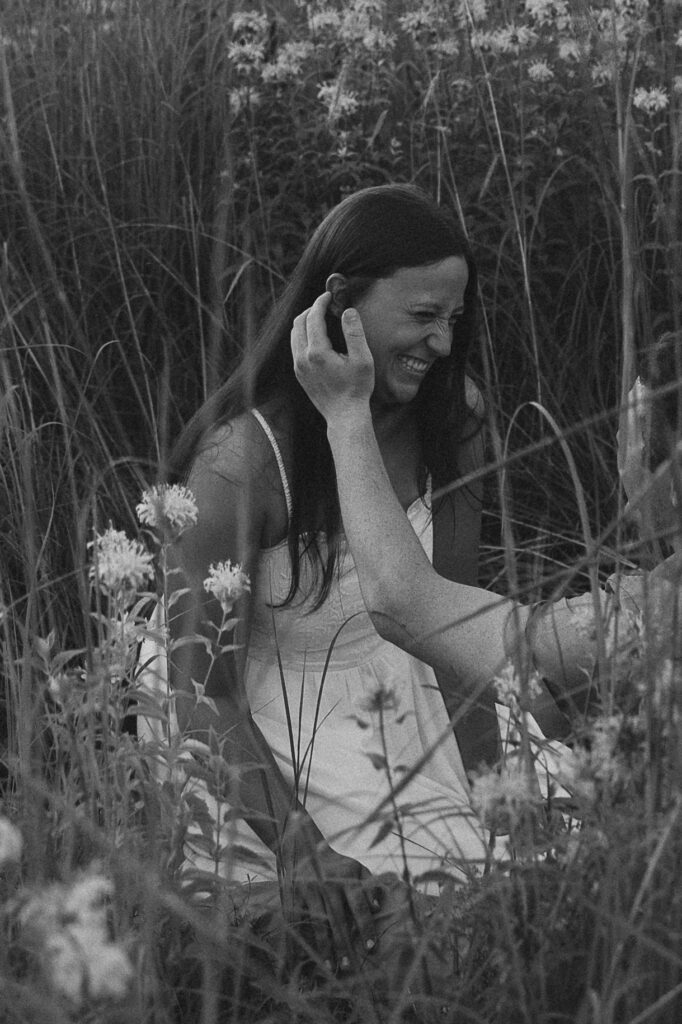 Sophie laughs through the wildflowers as Jake brushes a strand of hair from her face, a candid black-and-white frame that feels soft, honest, and full of real emotion.